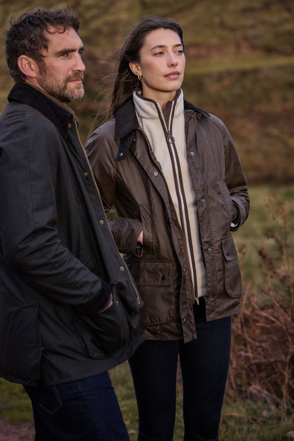 A man and woman in Barbour waxed jackets standing together on an autumn moor